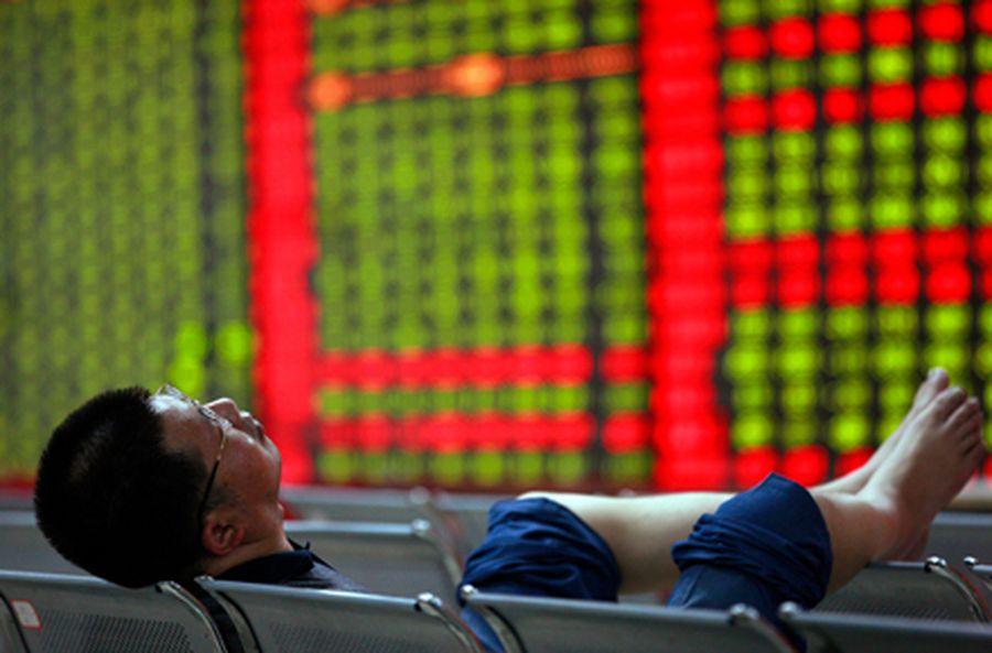 Investor sleeps on a bench in front of an electronic board showing stock information at a brokerage 