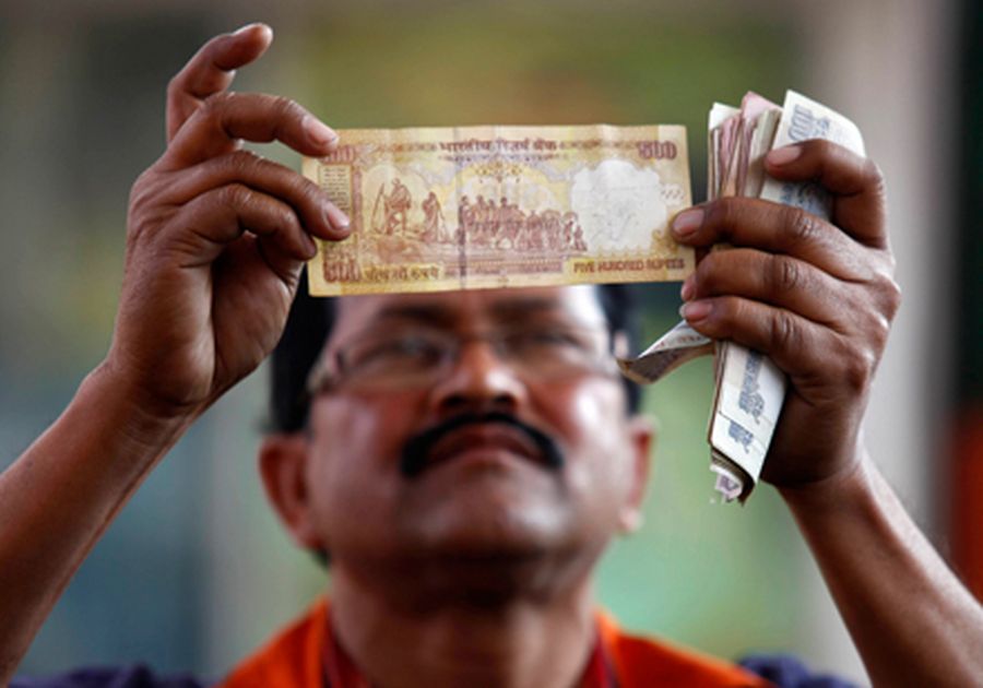 A worker at a fuel station checks a 500 Indian rupee note after filing a vehicle with fuel in Kolkat