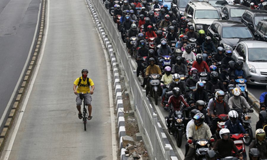 A man rides a bicycle in a bus lane next to a morning rush hour traffic jam in Jakarta