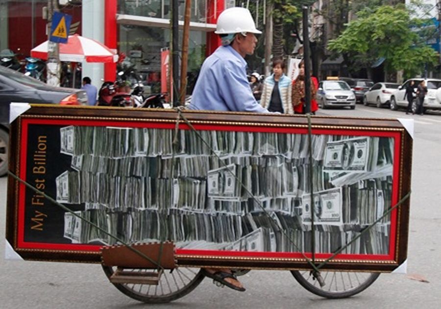 A man carries a billboard with an image of US-dollar notes as he rides a bicycle on a street in Hanoi. 