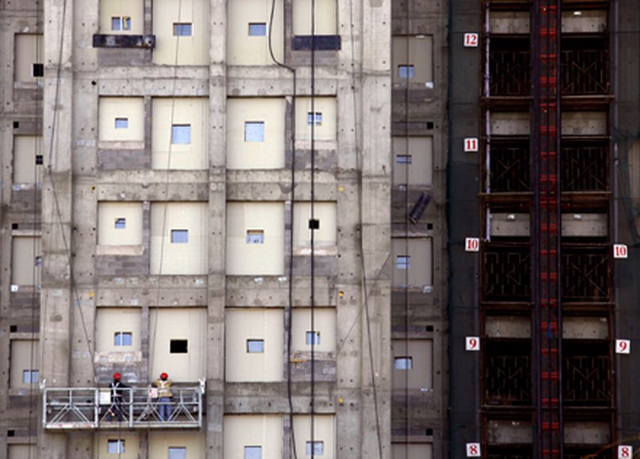 Construction workers stand on a platform as it hangs on the front of a new apartment block in Beijin