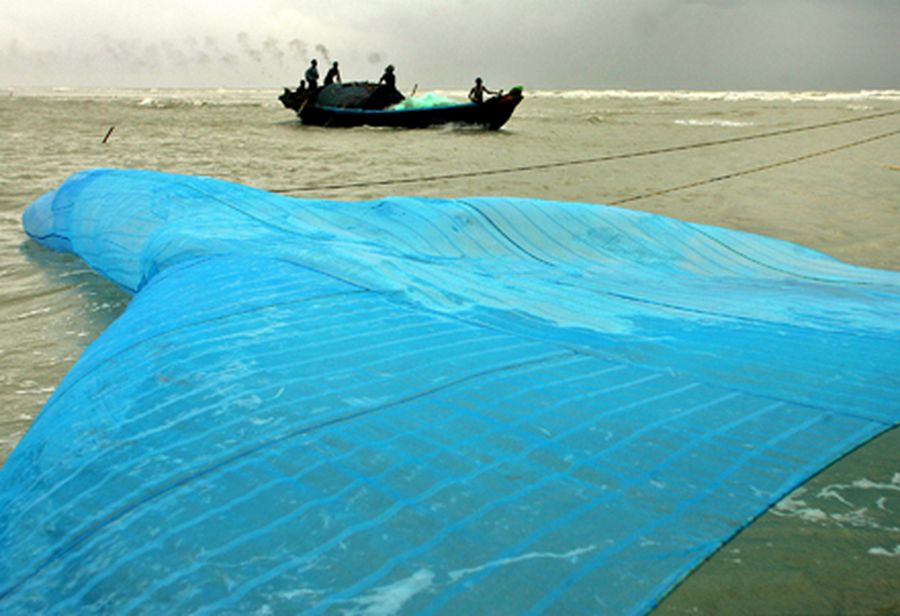 An Indian fishing boat crosses behind a giant fishing net in the backdrop of monsoon rain clouds at 