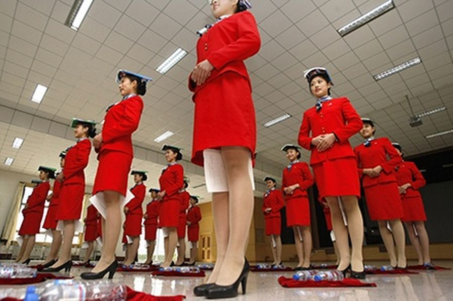 Students hold a piece of paper between their legs as they balance a book on their heads during etiquette training at a vocational school in Beijing.